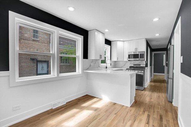 314 W 106th Pl, Chicago, IL 60628 - kitchen with stainless steel appliances, white cabinets, a peninsula, light countertops, and light wood-style flooring