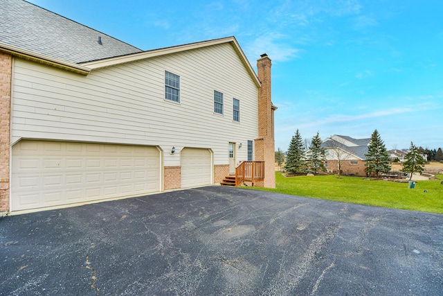 view of home's exterior featuring aphalt driveway, a shingled roof, an attached garage, a lawn, and brick siding