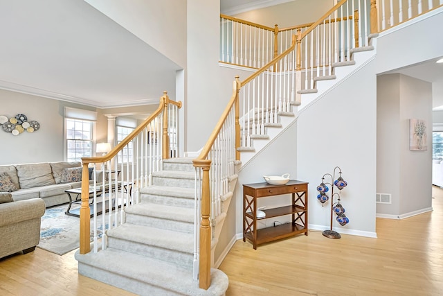 stairway with wood finished floors, a high ceiling, and ornamental molding