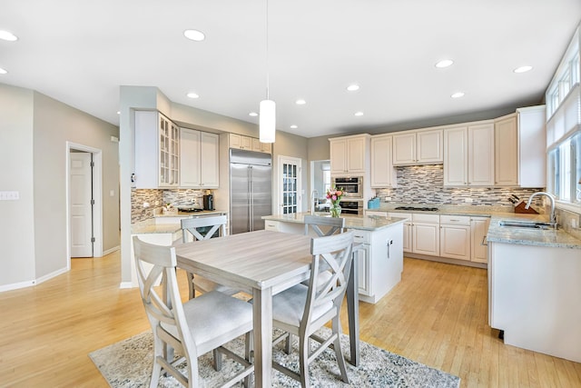 kitchen featuring stainless steel appliances, a center island, a sink, light wood-type flooring, and decorative backsplash