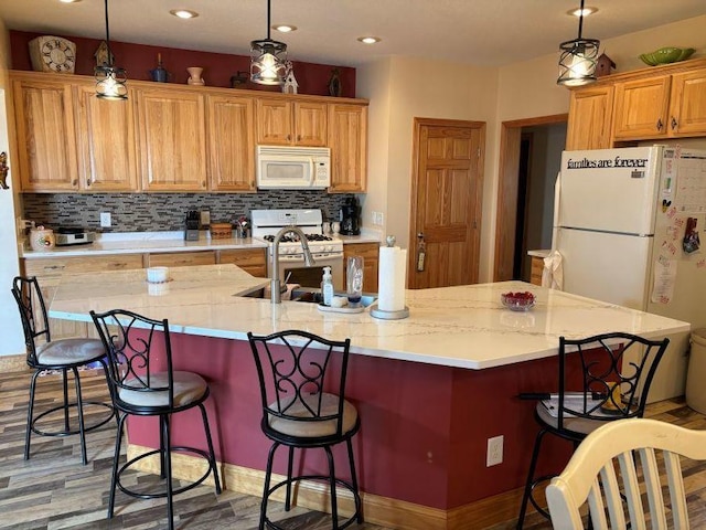 kitchen featuring tasteful backsplash, a large island with sink, a breakfast bar, white appliances, and decorative light fixtures