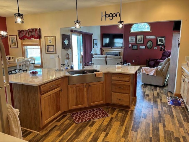 kitchen with dark wood-style floors, a sink, open floor plan, decorative light fixtures, and a fireplace