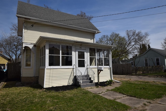 view of front of house with a sunroom, fence, roof with shingles, and a front yard