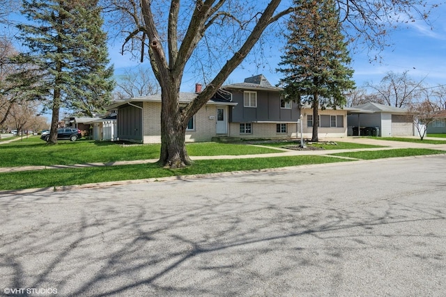 split level home featuring a chimney, a front lawn, driveway, a carport, and brick siding