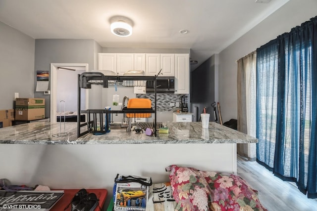 kitchen with stainless steel microwave, light wood-style flooring, light stone countertops, and white cabinets
