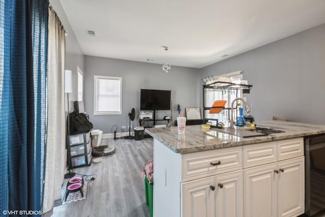 kitchen with white cabinets, light stone counters, wood finished floors, visible vents, and a sink