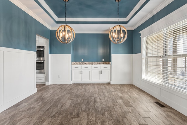 1101 Cascade Dr, Savoy, IL 61874 - unfurnished dining area featuring a chandelier, a tray ceiling, wood finished floors, crown molding, and wainscoting
