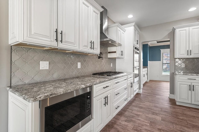 1101 Cascade Dr, Savoy, IL 61874 - kitchen featuring appliances with stainless steel finishes, wall chimney range hood, white cabinetry, dark wood-style flooring, and backsplash