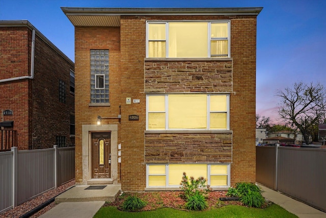 view of front of house featuring brick siding, fence, and stone siding
