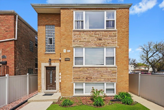 view of front facade featuring brick siding, fence, and stone siding