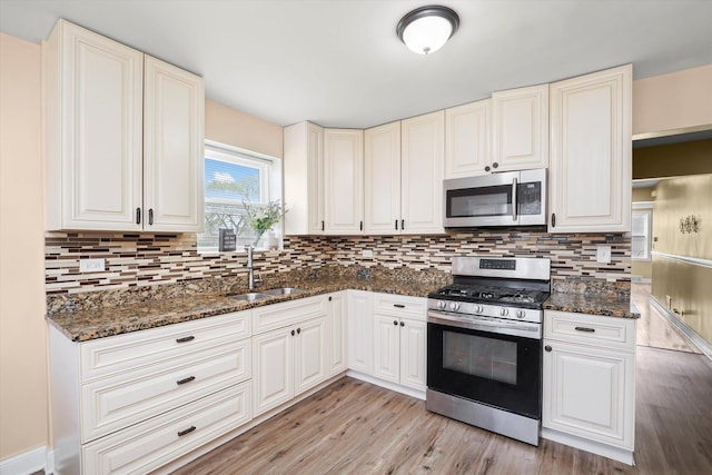 kitchen with backsplash, appliances with stainless steel finishes, a sink, and light wood finished floors