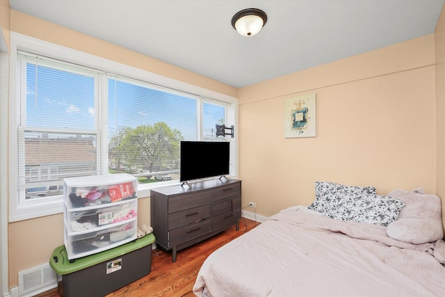 bedroom featuring baseboards, multiple windows, wood finished floors, and visible vents