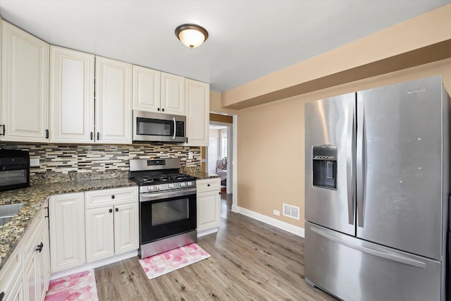 kitchen with decorative backsplash, visible vents, appliances with stainless steel finishes, baseboards, and light wood finished floors