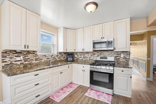 kitchen with stainless steel appliances, tasteful backsplash, a sink, and light wood-style floors
