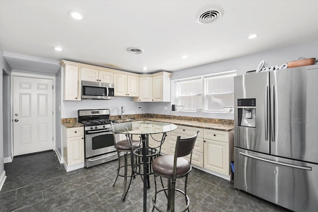 kitchen featuring cream cabinetry, stainless steel appliances, dark stone countertops, and visible vents