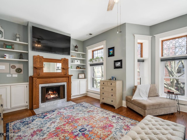 living area featuring ceiling fan, a fireplace, built in features, wood finished floors, and visible vents