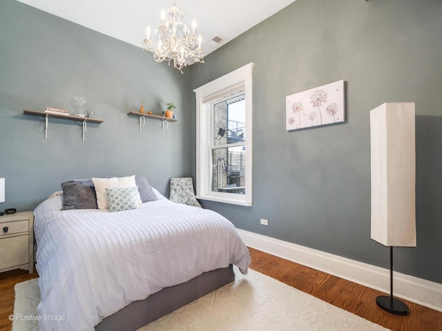 bedroom with visible vents, baseboards, wood finished floors, and a chandelier