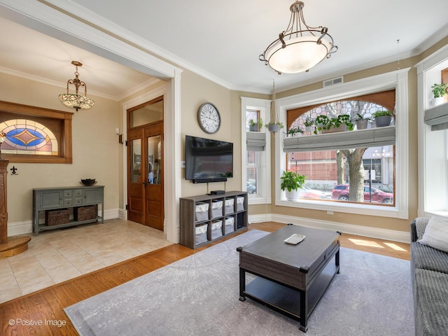 living area featuring visible vents, crown molding, wood finished floors, baseboards, and an inviting chandelier