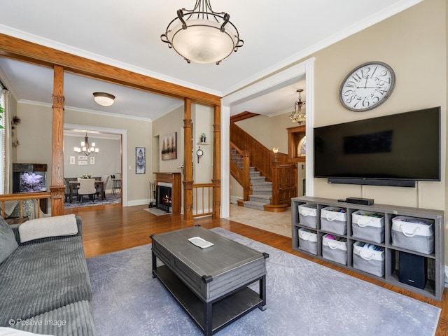 living room featuring a fireplace with flush hearth, crown molding, wood finished floors, stairway, and a chandelier