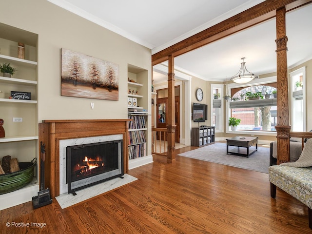 living area featuring crown molding, built in features, wood finished floors, baseboards, and a high end fireplace