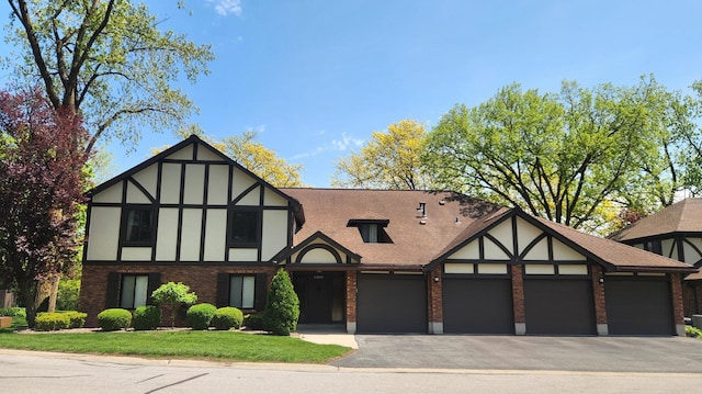 tudor-style house with brick siding, an attached garage, asphalt driveway, and a front lawn