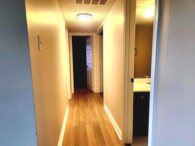 hall with light wood-type flooring, a textured ceiling, and baseboards