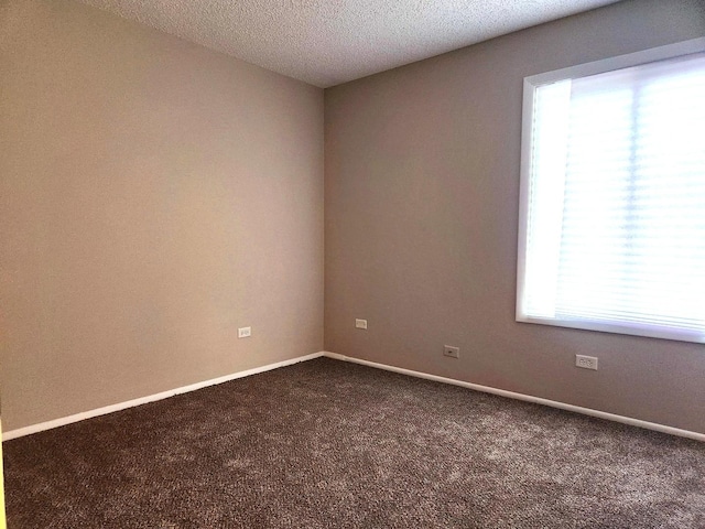 spare room with dark colored carpet, baseboards, and a textured ceiling