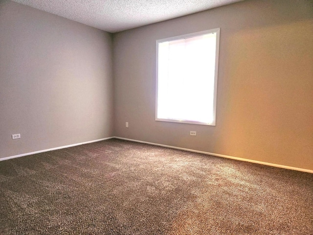 empty room featuring dark carpet, baseboards, and a textured ceiling