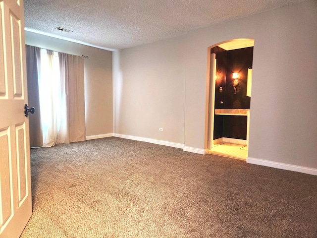 carpeted empty room with arched walkways, a textured ceiling, and baseboards