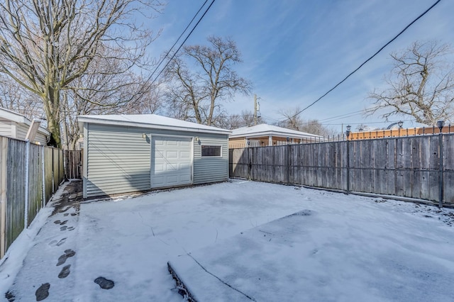 yard layered in snow featuring a garage, an outbuilding, and a fenced backyard