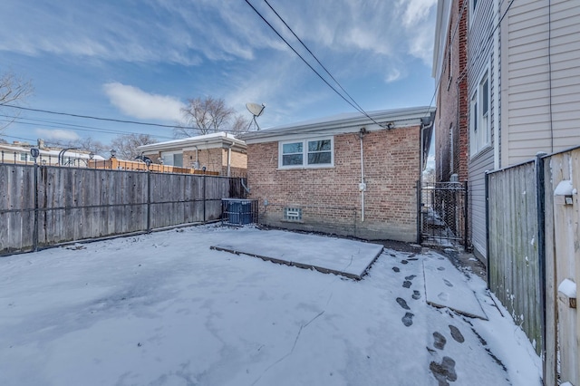 snow covered back of property featuring central AC, brick siding, and fence