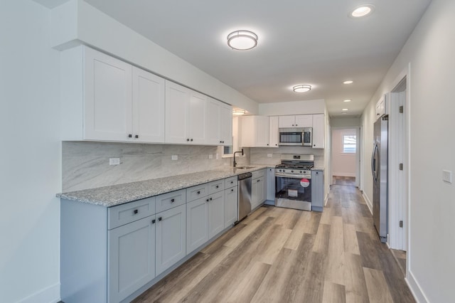 kitchen with a sink, white cabinetry, light wood finished floors, backsplash, and appliances with stainless steel finishes