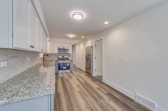 kitchen featuring stainless steel appliances, a sink, light wood-type flooring, visible vents, and white cabinetry