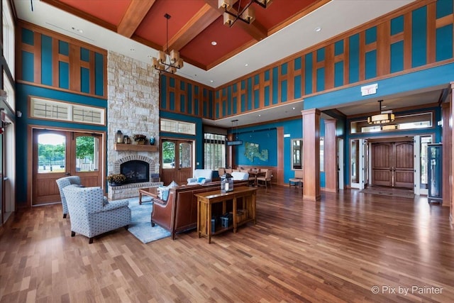 living room with a high ceiling, wood finished floors, beamed ceiling, a fireplace, and a notable chandelier