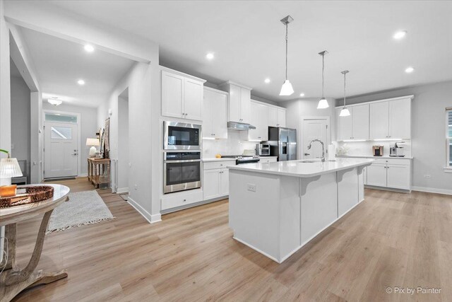kitchen with under cabinet range hood, light wood-style flooring, stainless steel appliances, and light countertops