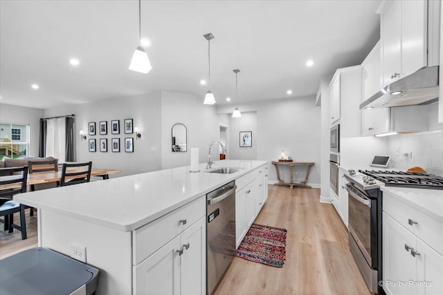 kitchen with a sink, light wood-style flooring, appliances with stainless steel finishes, a center island with sink, and under cabinet range hood