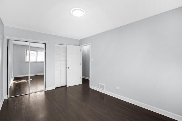 unfurnished bedroom with wood finished floors, baseboards, visible vents, and multiple closets