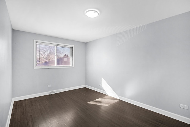 spare room with dark wood-type flooring, visible vents, and baseboards