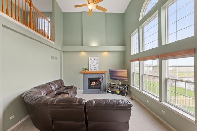 carpeted living area featuring a high ceiling, a fireplace, a ceiling fan, and visible vents
