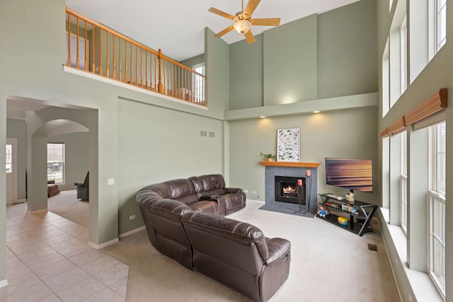 tiled living room with carpet flooring, a high ceiling, ceiling fan, and a fireplace