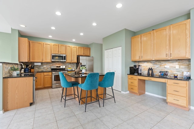 kitchen with appliances with stainless steel finishes, backsplash, light brown cabinetry, and a kitchen bar