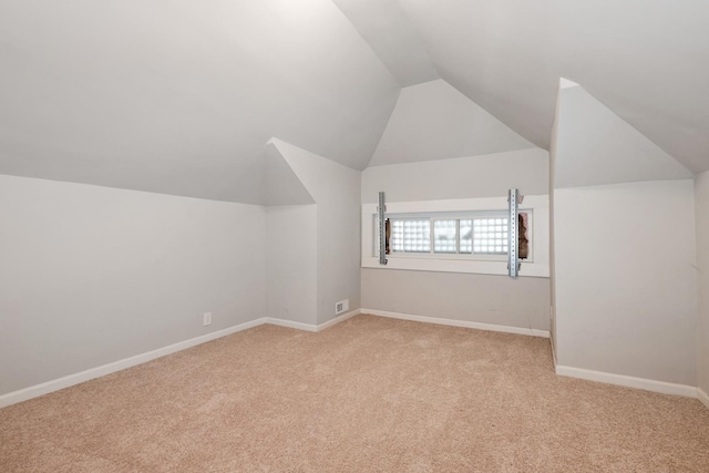 additional living space with visible vents, vaulted ceiling, light carpet, and baseboards