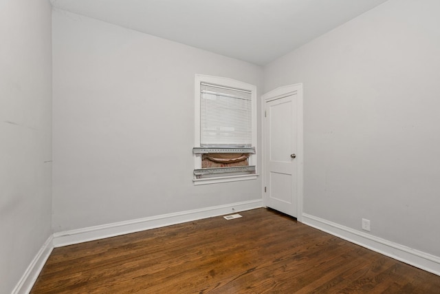 spare room featuring dark wood-type flooring, visible vents, and baseboards