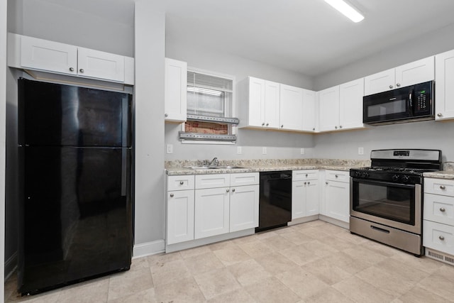 kitchen with black appliances, white cabinetry, light stone counters, and a sink