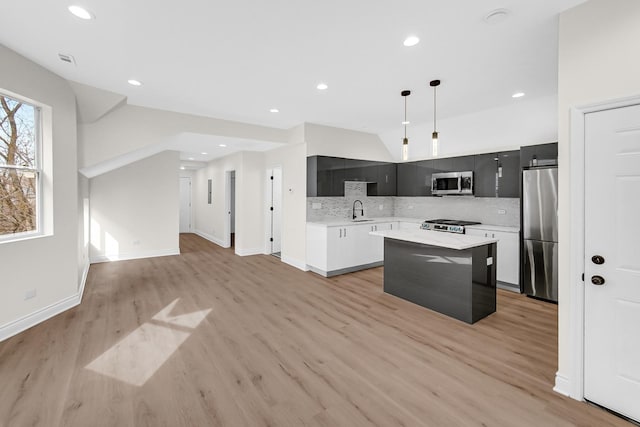 kitchen with stainless steel appliances, dark cabinets, light countertops, a sink, and light wood-type flooring