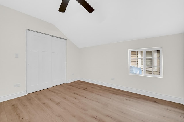 unfurnished bedroom featuring lofted ceiling, a ceiling fan, a closet, baseboards, and light wood-style flooring
