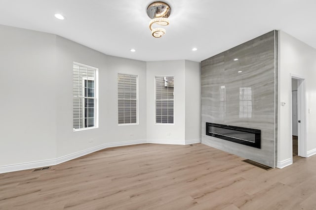 unfurnished living room featuring wood finished floors, a premium fireplace, baseboards, visible vents, and recessed lighting