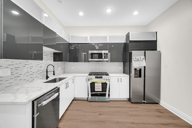 kitchen with light wood finished floors, stainless steel appliances, a sink, decorative backsplash, and light stone countertops