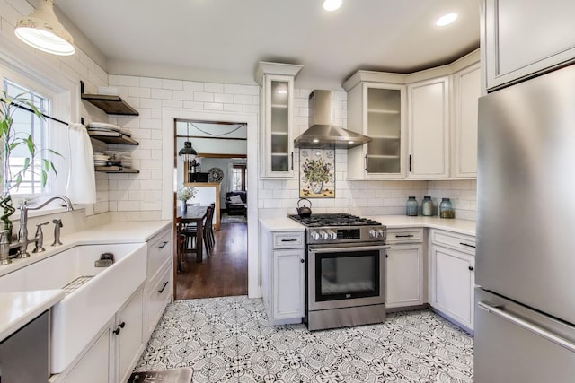 kitchen featuring open shelves, a sink, stainless steel appliances, light countertops, and wall chimney exhaust hood