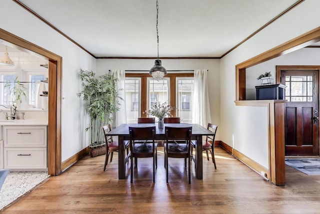 dining room featuring baseboards, crown molding, and light wood-type flooring